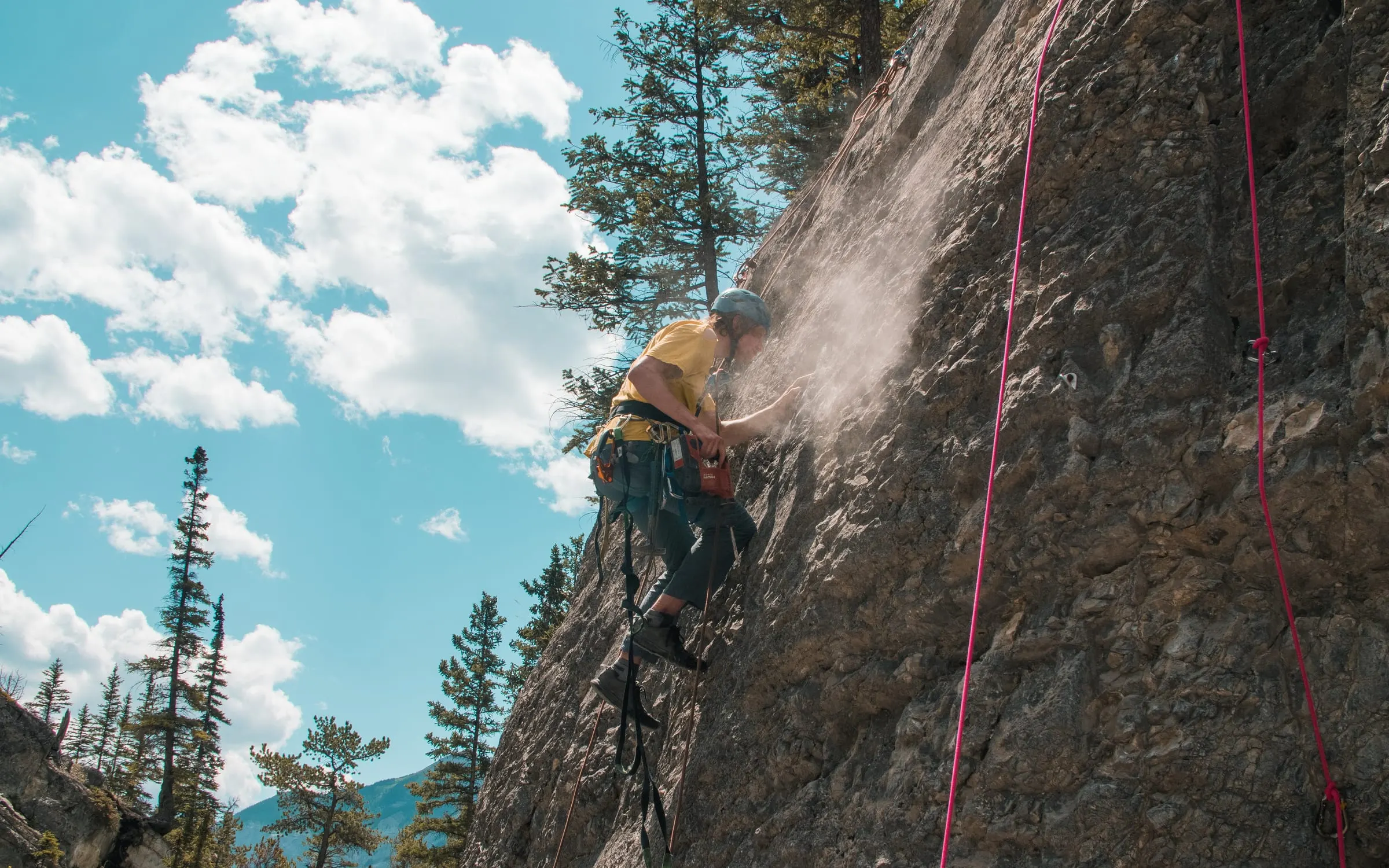 A volunteer hanging on a rope works on a limestone wall in a cloud of rock dust
