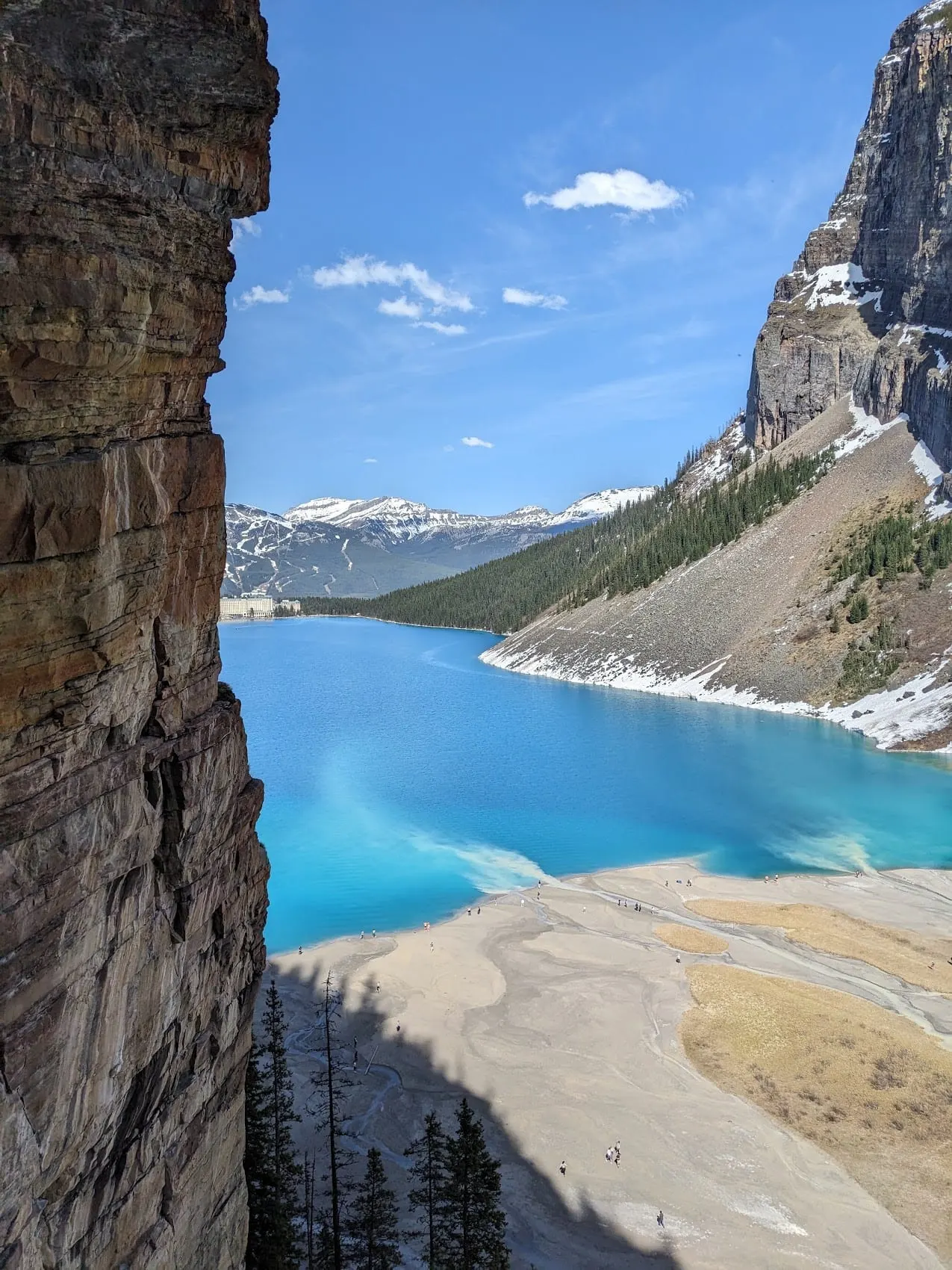 Turquoise Lake Louise seen from a cliff above the shore, with the Chateau at the far end of the lake