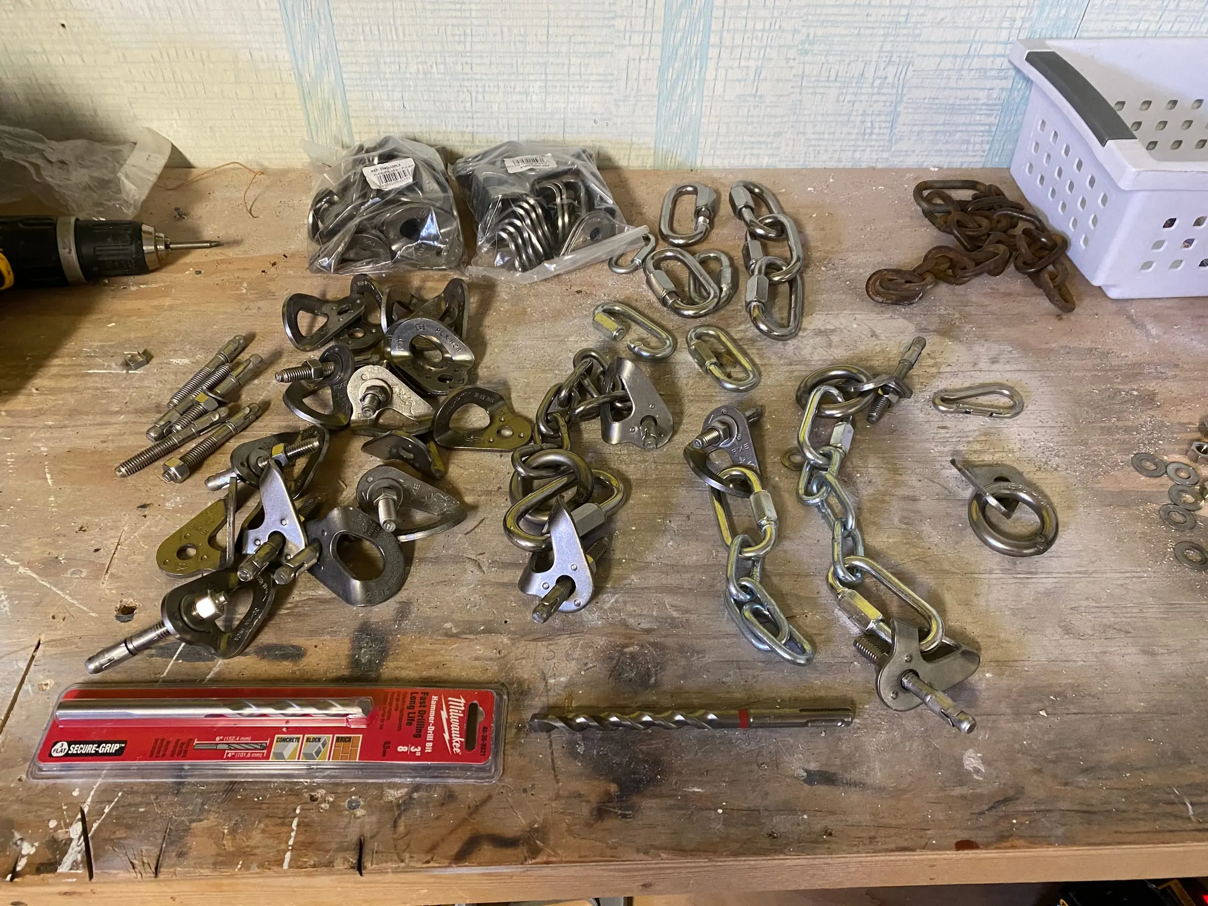 A workbench covered in new stainless steel hangers, bolts, quick links and chain, with a length of rusted old chain at the back